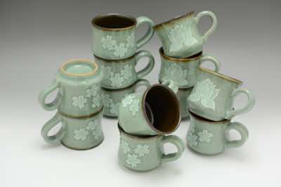 These cappuccino cups were hand-thrown and hand-carved with traditional Asian patterns.  The patterns include cherry blossoms, lotus flowers and water lilies (not shown).  Each cup is roughly 150ml (or 5oz) in volume.  Because celadon is a crackle glaze, dark tenmoku glaze is used for the interior of the cup instead.   